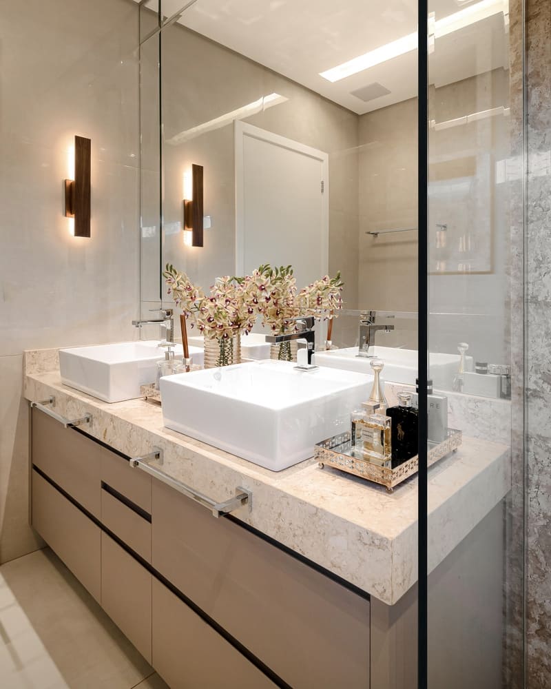 Bancada de banheiro em mármore com duas pias, iluminada por arandela da Accord.
