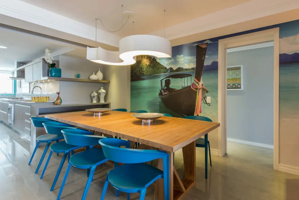 Sala de jantar com mesa de madeira, cadeiras azuis, parede com imagem de barco e Pendente Accord